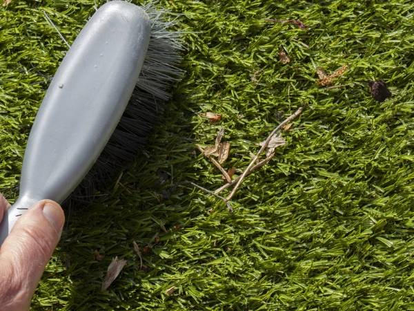 A hand is brushing the artificial grass with a brush.