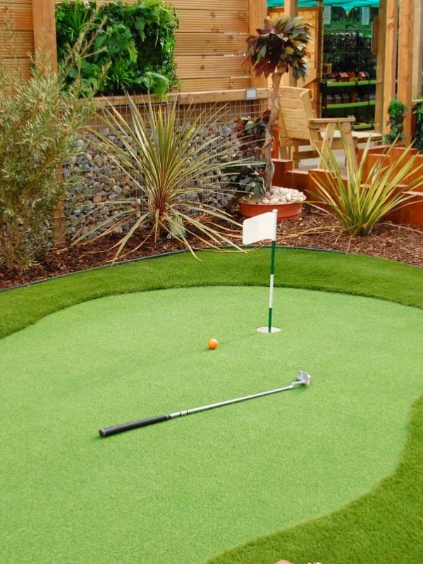 A golf and a golf club are placed on artificial grass putting green.