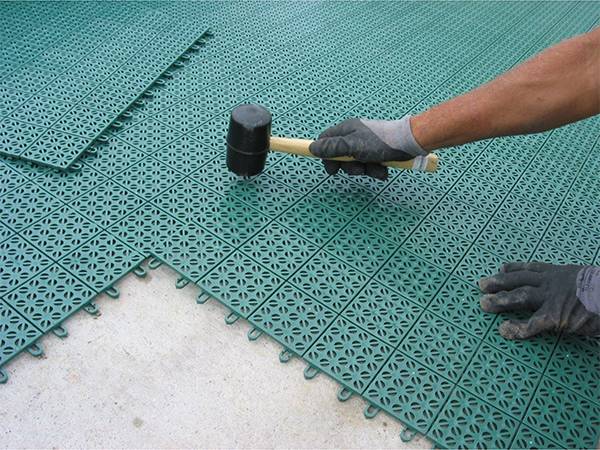 A man is installing interlocking sports flooring tiles by himself