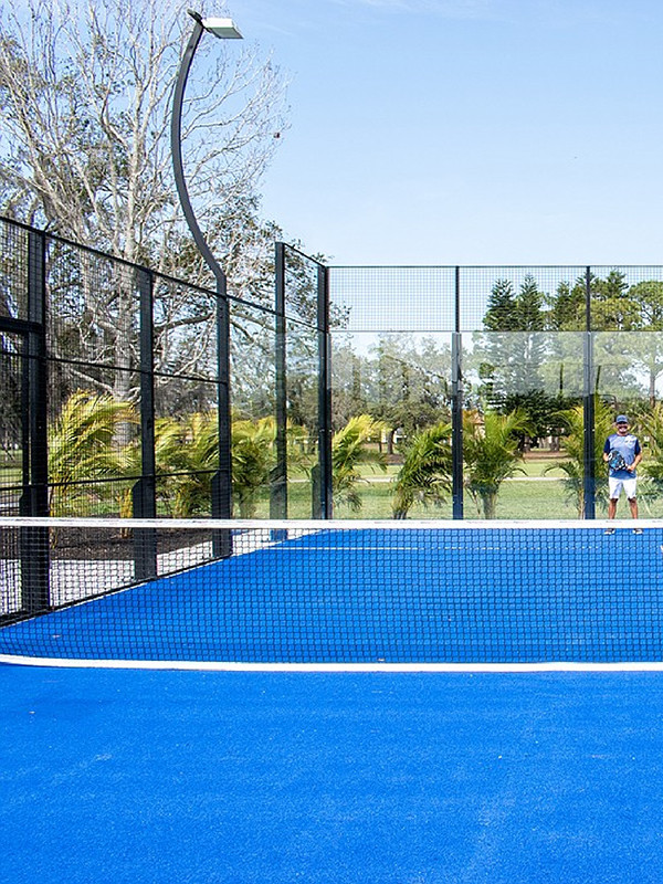 A person standing opposite the net of a panoramic padel court